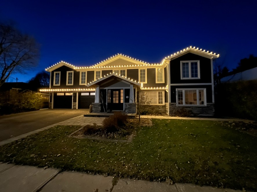 Split-level home with warm-white roofline lights at dusk